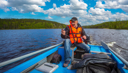 Man on motorboat. Guy floats down river. Tourist sits in blue motorboat. Boat driver uses electronic compass. Adult man in motorboat. Tourist in life jacket floats on lake. Summer forest behind guy
