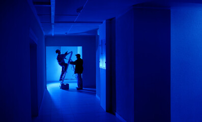 Workers in dark room. Corridor with builders near ladder. Lighting installation process....