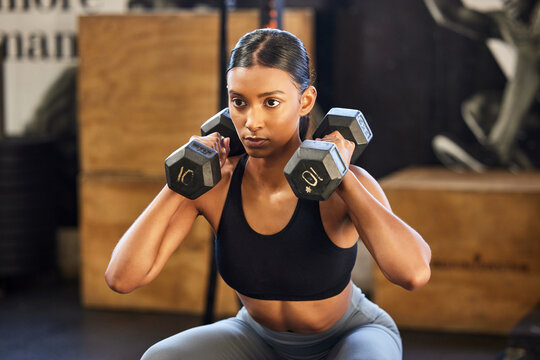 Fitness, squat or woman with dumbbells training, exercise or workout for powerful arms or muscles in gym. Dumbbell squats, bodybuilder or Indian girl athlete lifting weights or exercising biceps