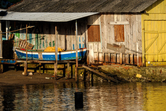 Casa velha de pescador &agrave; beira do rio com barco azul parado 