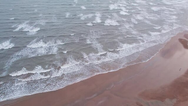 4K aerial shot of ocean waves crashing on sandy beach during day at Mandvi beach, Kutch, India. Beach background for summer vacation.