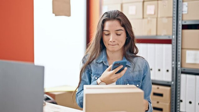 Young beautiful hispanic woman ecommerce business worker scanning package with smartphone at office