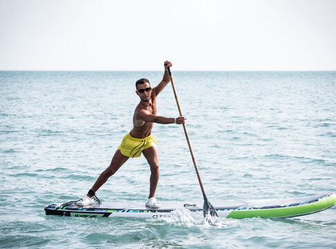 a sporty guy swims on a sup board with a paddle on the sea during the day against a beautiful sky