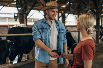A man with a leghorn is shaking hands with a blond woman with gloves working in a stall. - obrazy, fototapety, plakaty