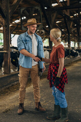 A man with a leghorn shakes hands with a woman working in a stable.