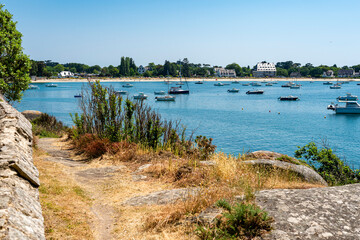 Summer stroll in Concarneau Bay, Brittany, France. The blue of the sky gives a beautiful emerald hue to the ocean. A few boats in and out of the bay.