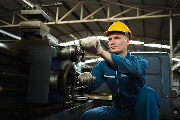 A male worker in a blue jumpsuit works in a metal lathe factory. The concept of working in a heavy metal industry factory.