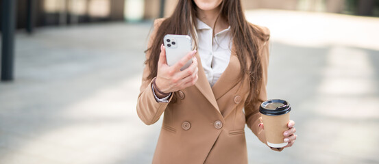 Businesswoman using her mobile phone while walking outdoor. Anonymous image, no face shown