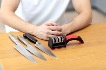 Close-up photo of man sharpening knives with special knife sharpener at home	