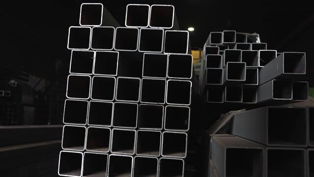 A stack of metal square tubes in a dark warehouse