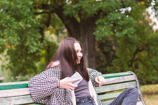 A relaxed young woman is sitting on a park bench with a satisfied expression on her face.