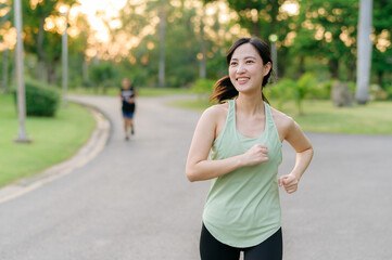 Fit Asian young woman jogging in park smiling happy running and enjoying a healthy outdoor...