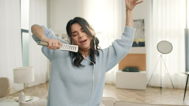 Portrait of happy crazy carefree latin american girl having fun in apartment. Slow motion funny hispanic woman dancing with hands. Joyful people lifestyle concept, dancing singing in hair brush mic 4K