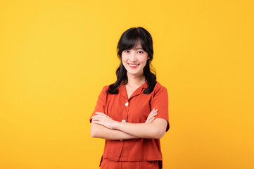 Portrait thoughtful young beautiful asian woman happy smile dressed in orange clothes showing thinking gesture isolated on yellow studio background.