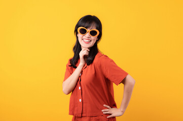 Portrait young beautiful asian woman cute and shy dressed in orange clothes and sunglasses touching cheeks showing shy emotional feeling isolated on yellow studio background.