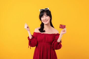 Portrait young beautiful asian woman happy smile dressed in red clothes showing credit card isolated on yellow background. Pay and purchase shopping payment concept.