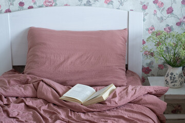Bed in bedroom. Flowers wallpaper. Book on white bed.