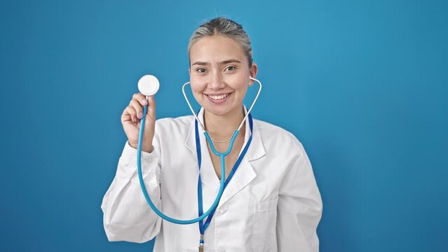 Young beautiful hispanic woman doctor smiling confident holding stethoscope over isolated blue background