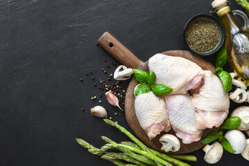 Fresh pieces of chicken thigh meat on wooden cutting board with ingredients for cooking healthy...