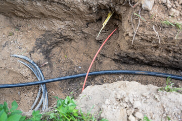Different cables for electricity and fiber optics are lying jumbled in the ground near a house,...