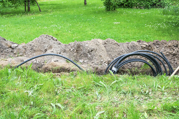Black power cable is laid in a narrow trench in the grass across the garden, because it is a safer power supply than overhead lines, copy space, selected focus - 609708645