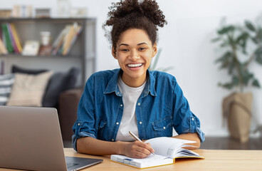 Happy female student using laptop computer, studying, distance learning or online education, looking at the camera smiling friendly. African American woman freelancer working from home