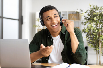 Mixed race man in headset, office employee or call center worker sitting in a modern office and talking to a client, smile