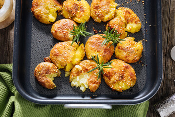 Baked potatoes in metal tray seasoned with rosemary and salt and pepper. Golden and crispy.
