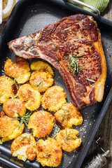 Prime cut of steak with baked potatoes served in metal tray. Seasoned with rosemary, pepper and garlic. Juicy and delicious