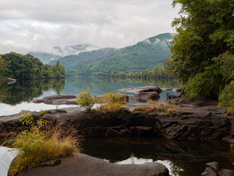 Fluvial landscape of the confluence of the Mi&ntilde;o and Avia rivers, in Ribadavia Orense, with the green mountains and the sky reflected in the transparent water and  rocks in the water summer 2021 Spain.