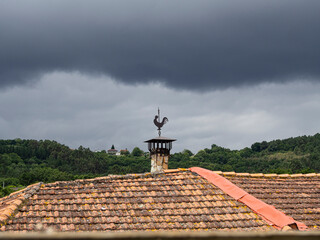 Dark storm cloud, with a rooster-shaped weather vane on an ocher roof.