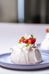 Two small pavlova cakes from meringue decorated with fresh strawberries on a pink plate. Bright scene with flowers as decoration.
