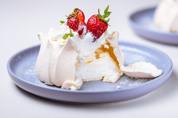 Two small pavlova cakes from meringue decorated with fresh strawberries on a pink plate. Bright scene with flowers as decoration.