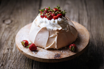 Pavlova cake decorated with strawberries in rustic, wooden atmosphere. Cake is made from meringue and whipped cream