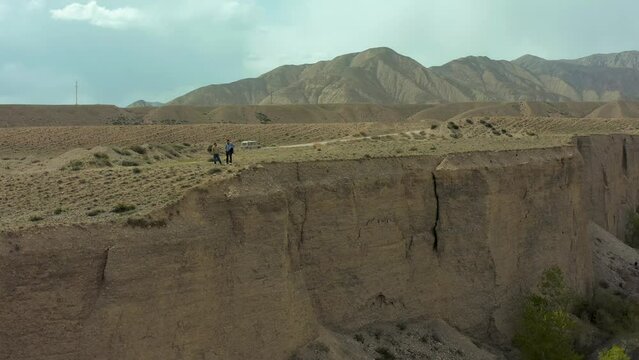 Aerial view of couple people standing on edge of  mountain range. Bird's eye view from drone along scenic sandy canyon. Kyrgyzstan, Central Asia. Epic scenery and breathtaking views of highland.
