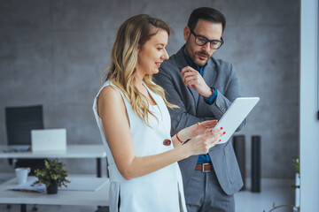 Businessman and businesswoman smiling looking at tablet PC in modern office and coworking space. Business people in the office. Shot of two young colleagues having a discussion in modern office.