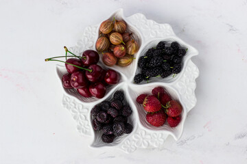 Berry plate on a white background. Strawberries, gooseberries, cherries, raspberries and mulberries
