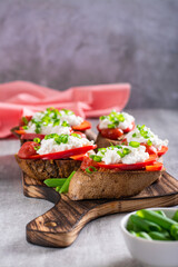 Delicious crostini with baked tomatoes, bell peppers, ricotta and herbs on a board vertical view