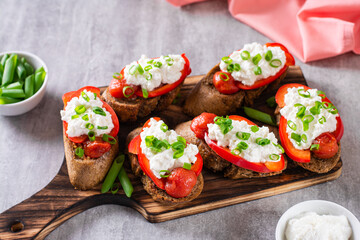 Bruschetta on rye bread with ricotta, pepper, tomato and green onion on the board