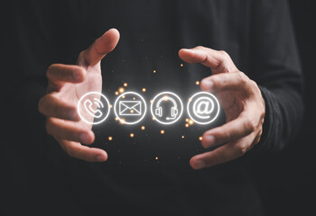 Hand holds phone, mail, and message icons, symbolizing contact and communication. Customer service call center and feedback on black background. Business concept. Communication, contact, and feedback