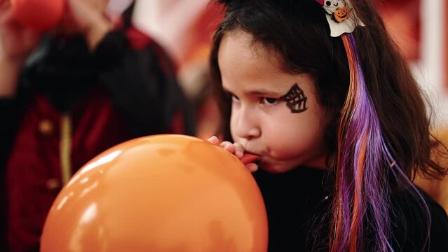 Adorable hispanic girl having halloween party inflating balloon at home