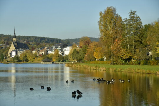 Le lac des Doyards et le village de Vielsalm avec l'&eacute;glise paroissiale Saint Gengoux se refl&eacute;tant dans ses eaux  sous un ciel clair d'automne 