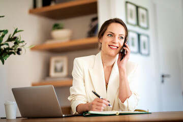 Happy businesswoman having a phone call and using laptop for work
