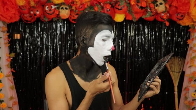Brown-skinned boy putting on makeup for halloween party. Scary decoration.