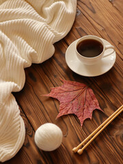 Knitting needles, ball of wool, cup of coffee and autumn leave on wooden background
