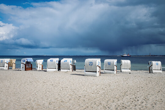 Sandy beach on the coast of the Baltic Sea in Strande / Kiel in Germany. With several beach chairs, a ferry and dark clouds after a rain shower.