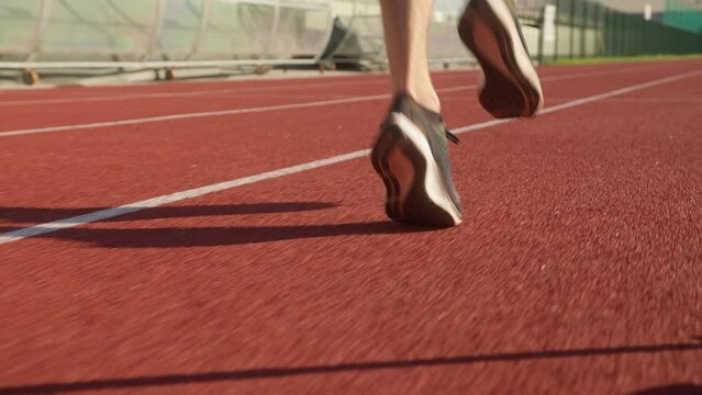 Rear view of male athlete&rsquo;s lower legs and feet in sneakers running elegant along an athletic track, tracking shot.