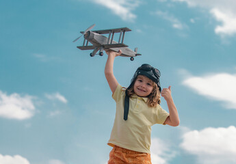Child boy with pilot goggles and helmet playing with wooden toy airplane. Kid dreams of future. Kid pilot dreaming. Childhood dream concept. Blonde cute daydreamer child dream on fly.