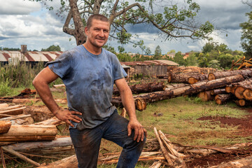 Polish immigrant man working in a sawmill, smiles looking at the camera, his clothes are dirty and worn from work.