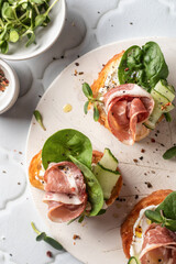 Bruschetta with ham or prosciutto, cream cheese, cucumber, spinach and microgreens. Tasty sandwich or toasted bread on white tray, appetizer or breakfast. Top view, flat lay